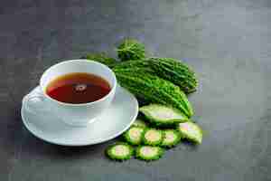 Free photo a cup of hot bitter gourd tea with sliced raw bitter gourd place on dark floor