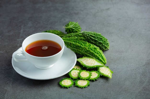 a cup of hot bitter gourd tea with sliced raw bitter gourd place on dark floor