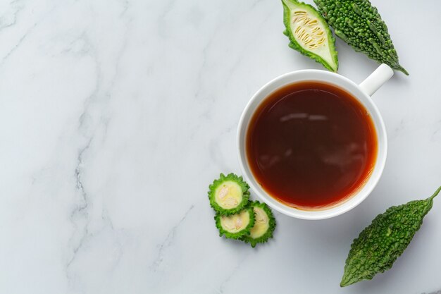 a cup of hot bitter gourd tea with sliced raw bitter gourd place on white marble floor