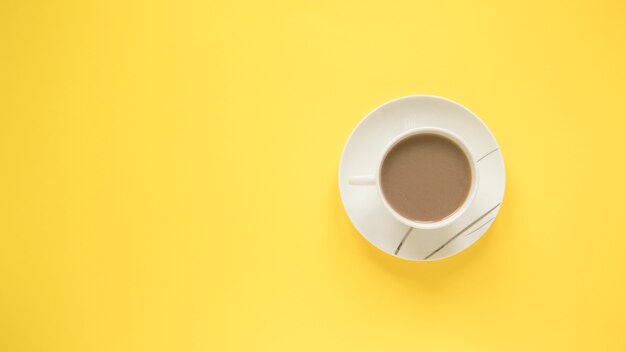 밝은 노란색 배경 위에 접시와 뜨거운 커피 한 잔
