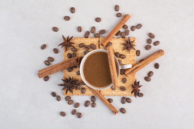 A cup of hot coffee with star anise and cinnamon sticks on crackers