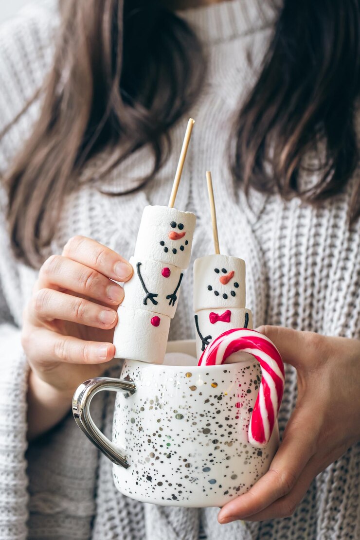 Free Photo cup of hot drink with marshmallow snowmen and candy in female hands
