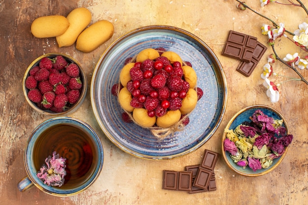 A cup of hot herbal tea soft cake with fruits chocolate bars on mixed color table