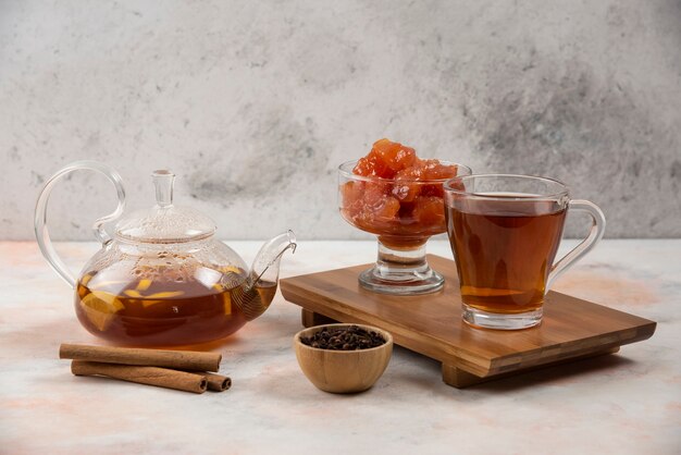 Cup of hot tea, teapot and sweet quince jam on wooden board. 