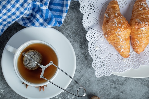Cup of hot tea with delicious croissants on marble surface.