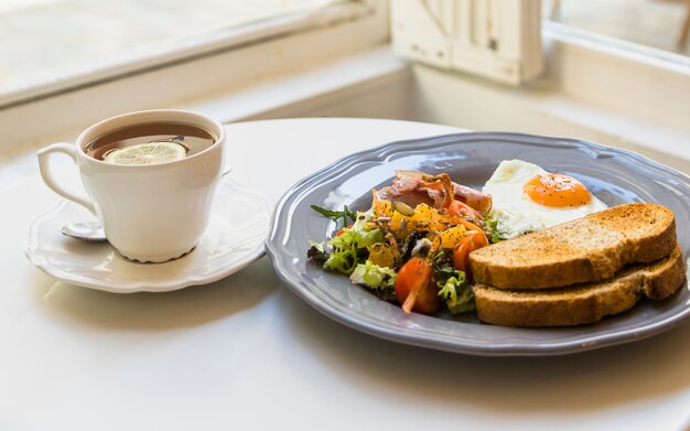 Cup of lemon tea and breakfast on round white table