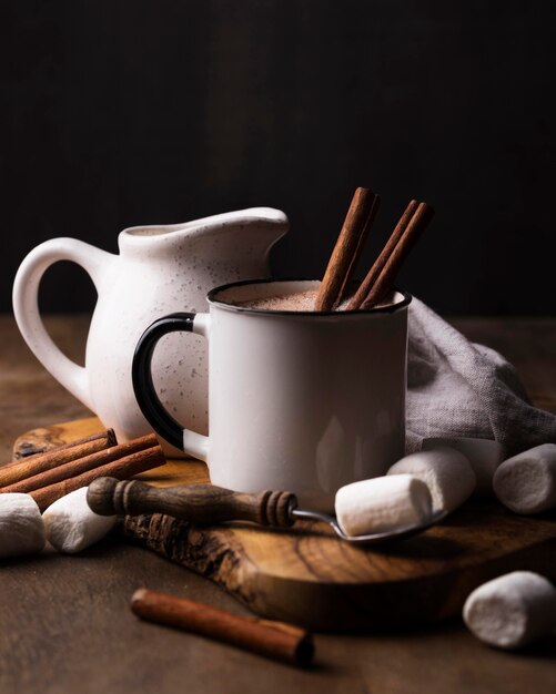 Cup of marshmallow drink with cinnamon on wooden board