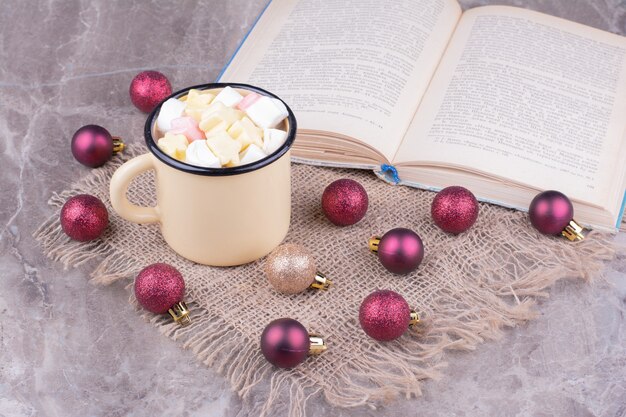 A cup of marshmallow drink with red christmas tree balls around