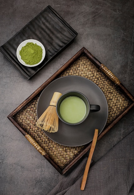 Cup of matcha tea on tray with bamboo whisk
