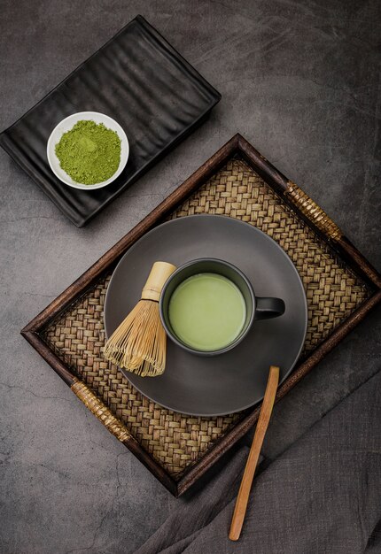 Cup of matcha tea on tray with bamboo whisk