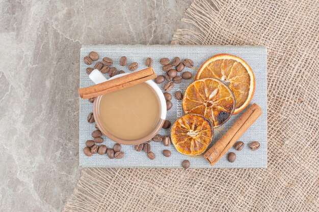 Чашка кофе с молоком с кофейными зернами и дольками апельсина на книге. Фото высокого качества