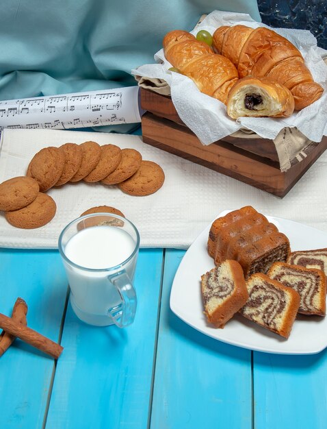 A cup of milk with cinnamon sticks and pastries on the table.