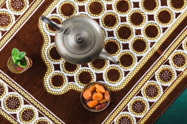 Cup near retro teapot and dried fruits on mat