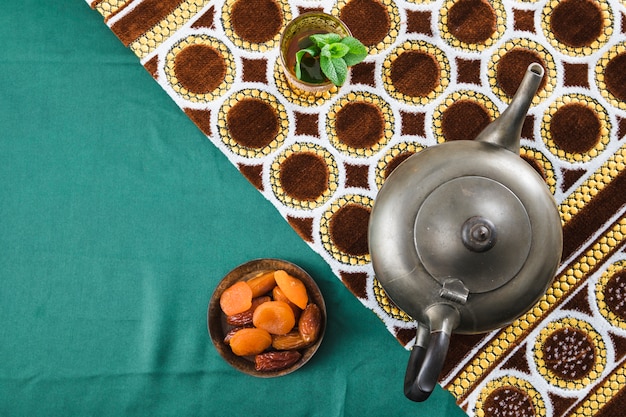 Cup near retro teapot and dried fruits near mat on wrinkled material