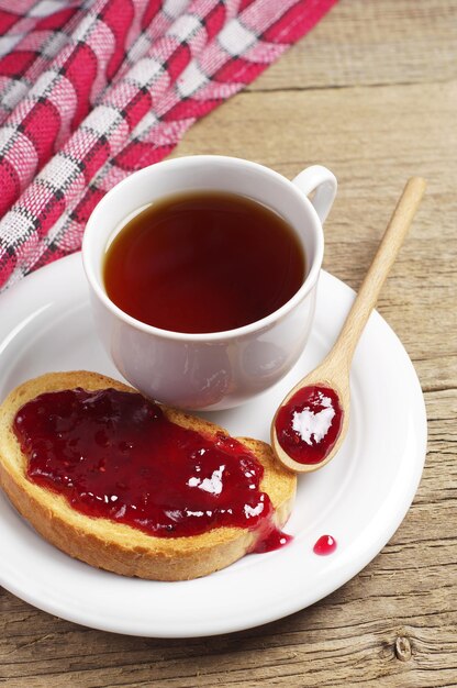 오래된 나무 테이블에 접시에 잼을 넣은 뜨거운 차 한 잔과 튀긴 빵 프리미엄 사진