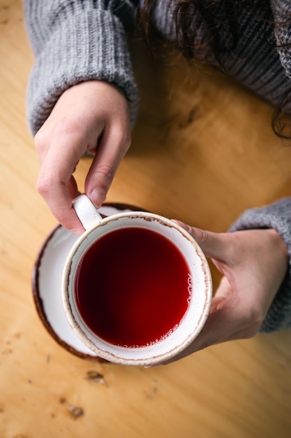 Чашка чая красного цвета в женских руках вид сверху