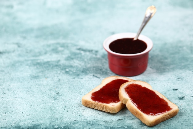 A cup of red jam with two slices of bread.