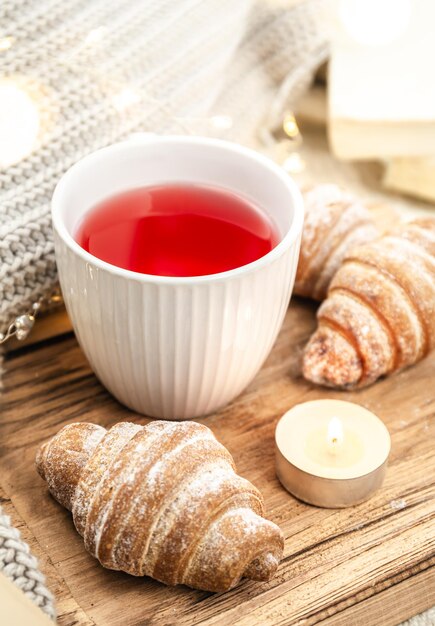 Foto gratuita una tazza di tè rosso, una candela, un croissant e un elemento lavorato a maglia su un vassoio a letto