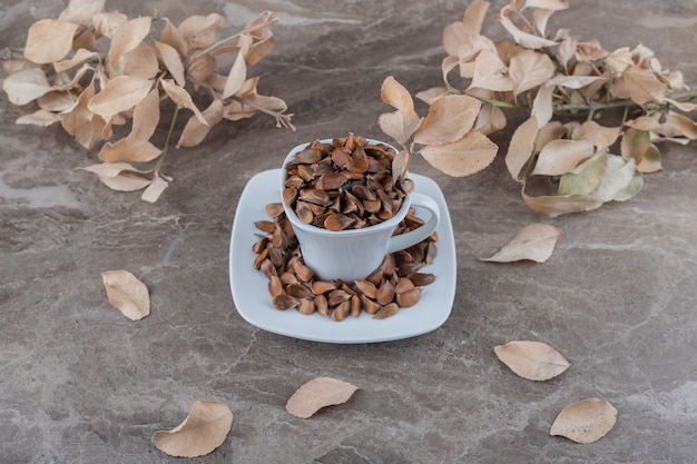 A cup of seeds in front of leaves on the marble surface