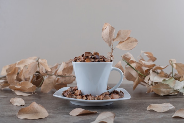 A cup of seeds in front of leaves on the marble surface