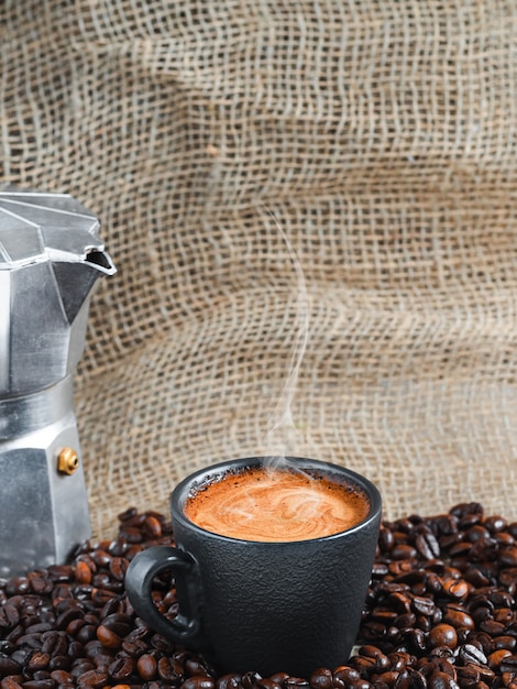 커피 포트 옆에 볶은 커피 원두 사이에 거품이있는 강한 향이 나는 에스프레소 커피 한잔