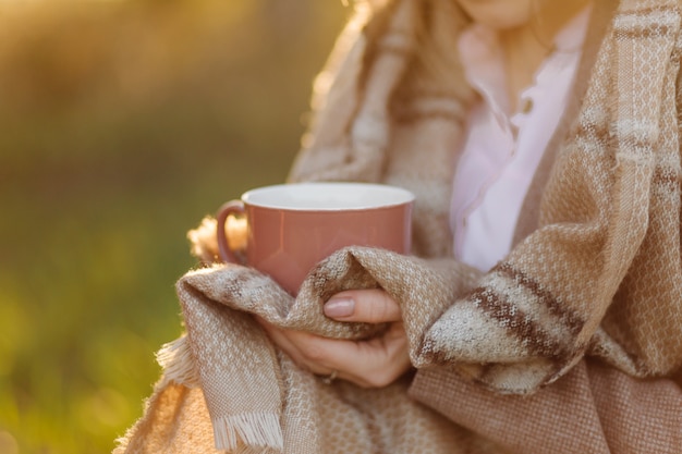 Cup on sunset in hand young girl covered with a blanket