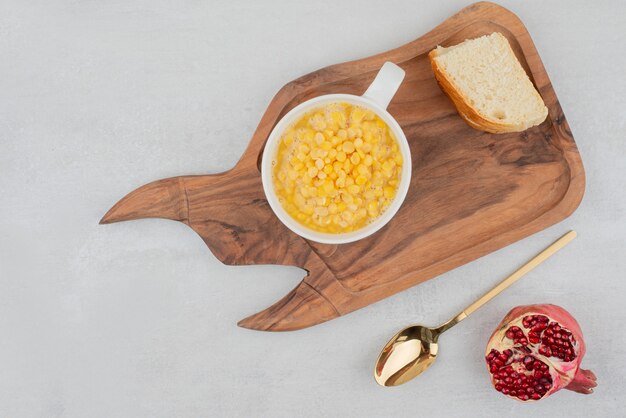 Cup of sweet corn with bread slice on wooden board