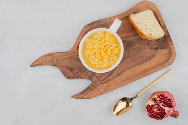 Чашка сладкой кукурузы с ломтиком хлеба на деревянной доске