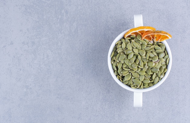 A cup of tasty pumpkin seeds with dried lemon on marble.