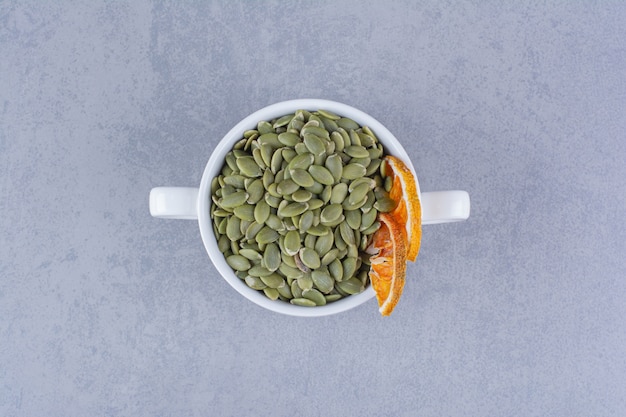A cup of tasty pumpkin seeds with dried lemon on marble.