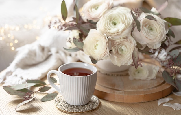 Free photo a cup of tea and a bouquet of ranunculus flowers on a blurred background