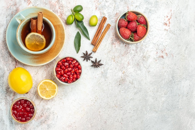 a cup of tea bowls of berries lemon star anise and cinnamon sticks next to the cup of tea with cinnamon on the table