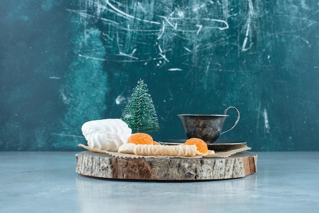 Cup of tea, bundle of desserts and a tree figurine on a wooden board on marble.