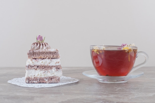 A cup of tea and a cake slice on a doily on marble 