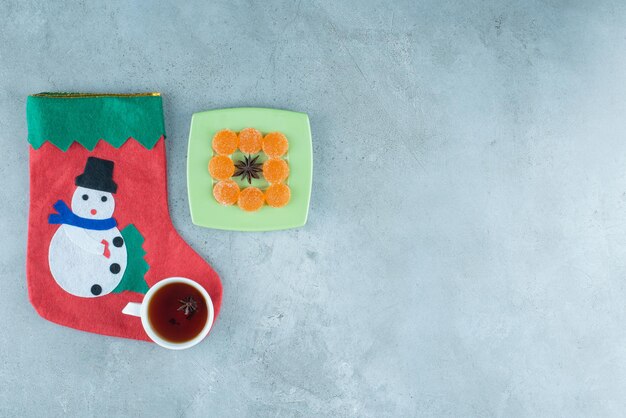 대리석 접시에 있는 아니스 주위의 마멜레이드 옆에 있는 차 한 잔과 크리스마스 양말.