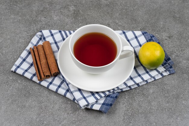 Cup of tea, cinnamon sticks and lemon on marble surface