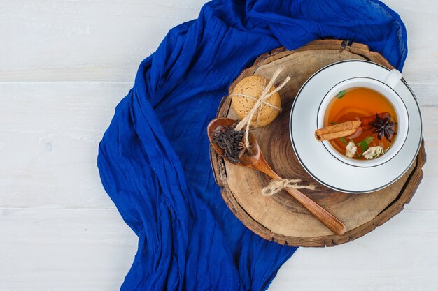 Cup of tea, cloves and cookies on wooden board with blue scarf