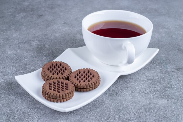 Cup of tea and cocoa biscuits on white plate