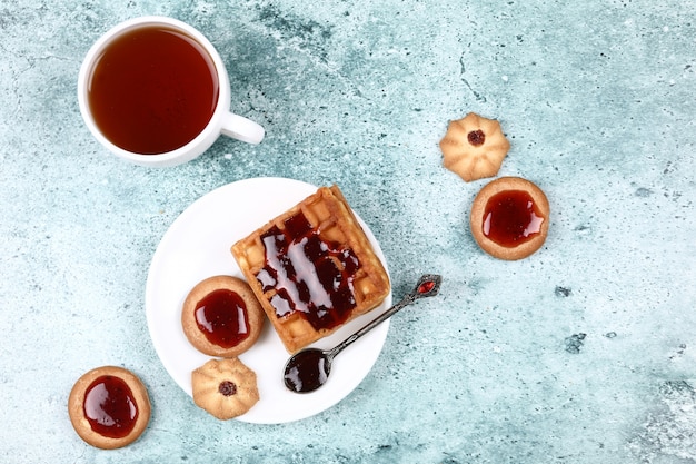 Foto gratuita una tazza di tè, biscotti e waffle con marmellata di fragole.