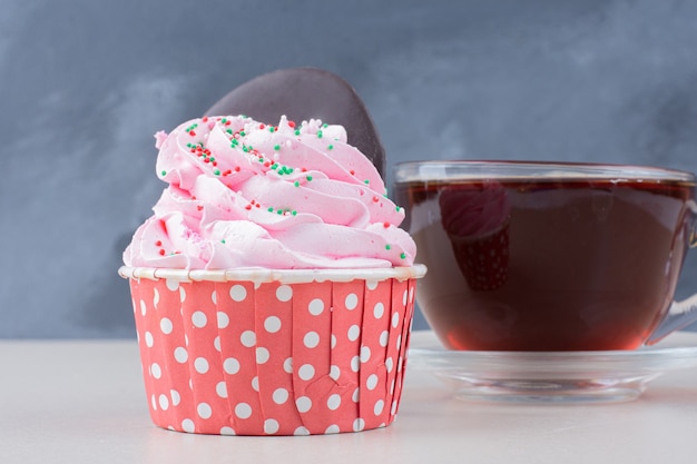 A cup of tea and cupcake on white table.