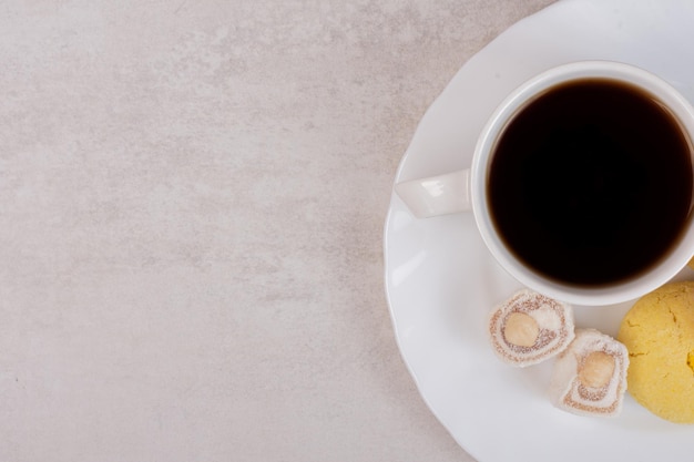 Cup of tea, delights and cookie on white table.