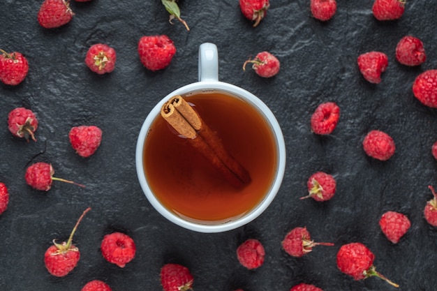 Cup of tea and fresh raspberries on black table. 