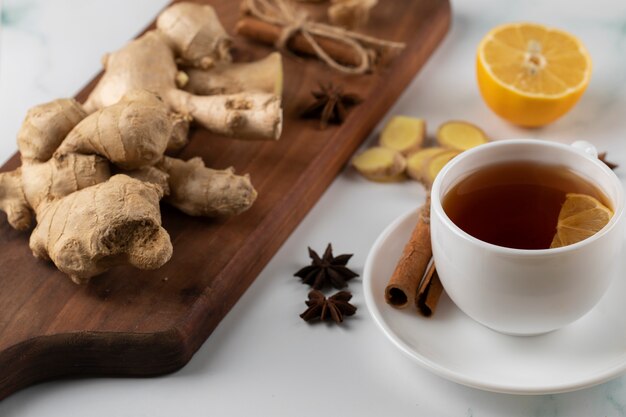 A cup of tea and ginger plants on a wooden board.