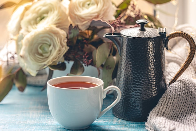 Чашка чая, чайник и цветы у окна.