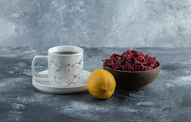 Cup of tea, lemon and bowl of dried flowers on marble table. 