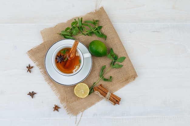 Free photo a cup of tea,limes and cinnamon in a linen placemat