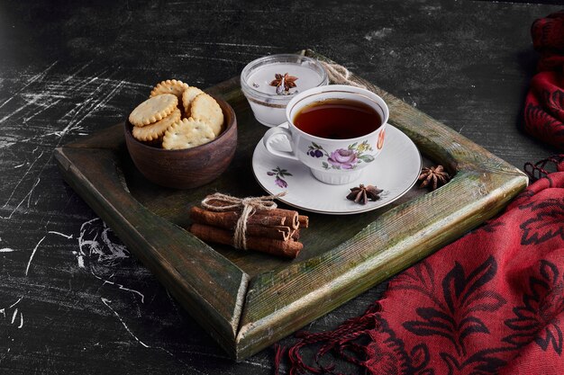 A cup of tea in a metallic tray with cookies. 