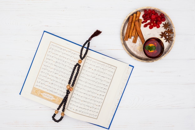 Cup of tea near spices on tray and book with beads