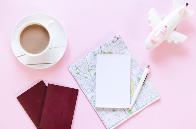 Cup of tea; passport; map; paper; pen and airplane on pink backdrop