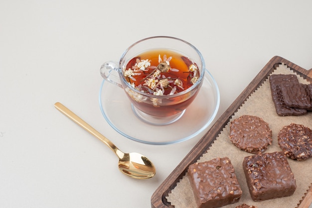 Cup of tea and plate of chocolate cookies on white surface